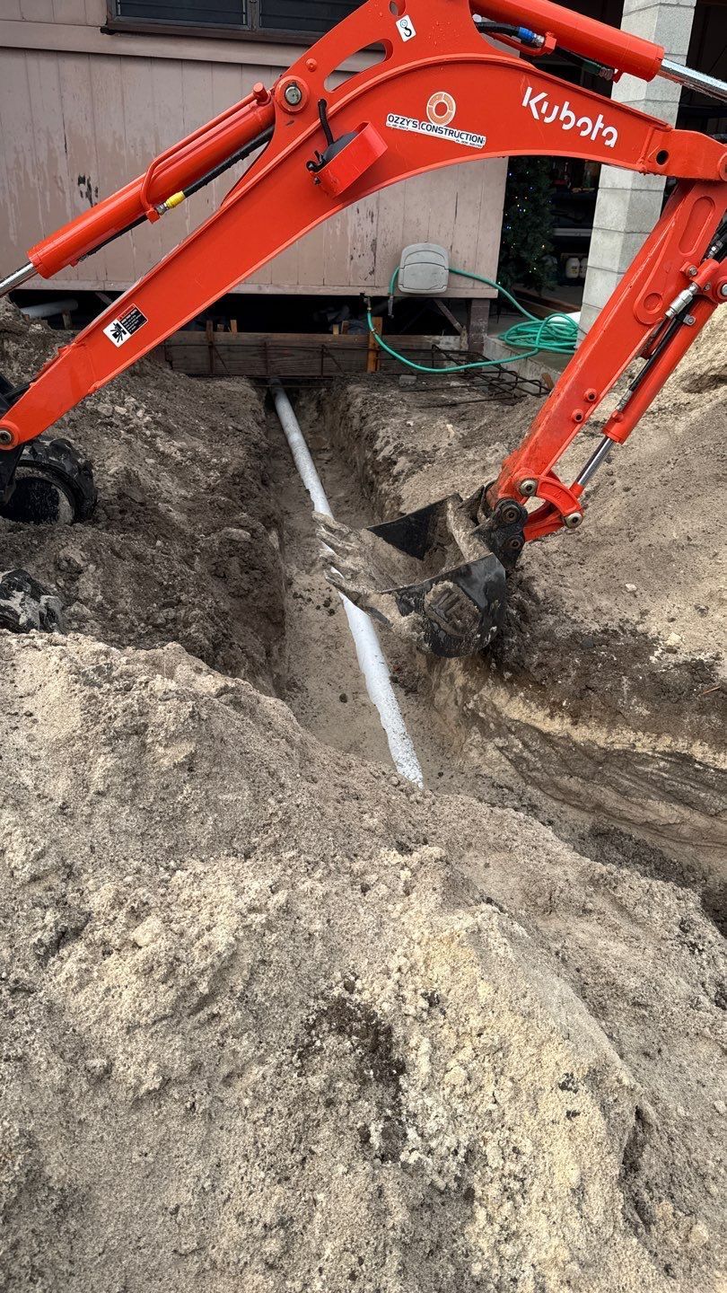 Orange excavator digging a trench around a white pipe at a construction site.