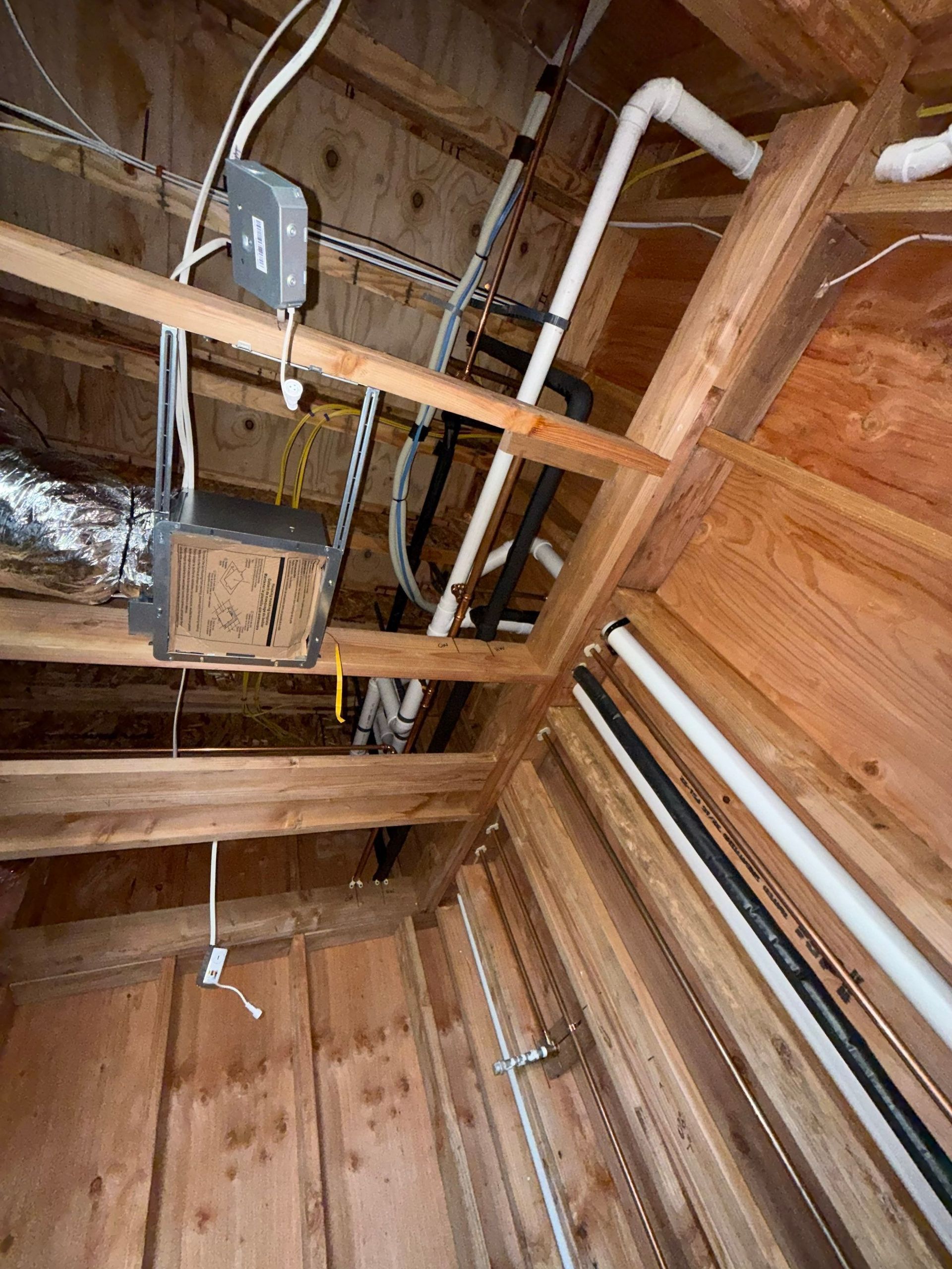 Attic framing with exposed wooden rafters, insulation, and electrical wiring.