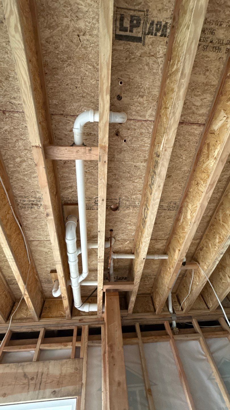 Exposed attic ceiling framing with white PVC pipes running between wooden joists.