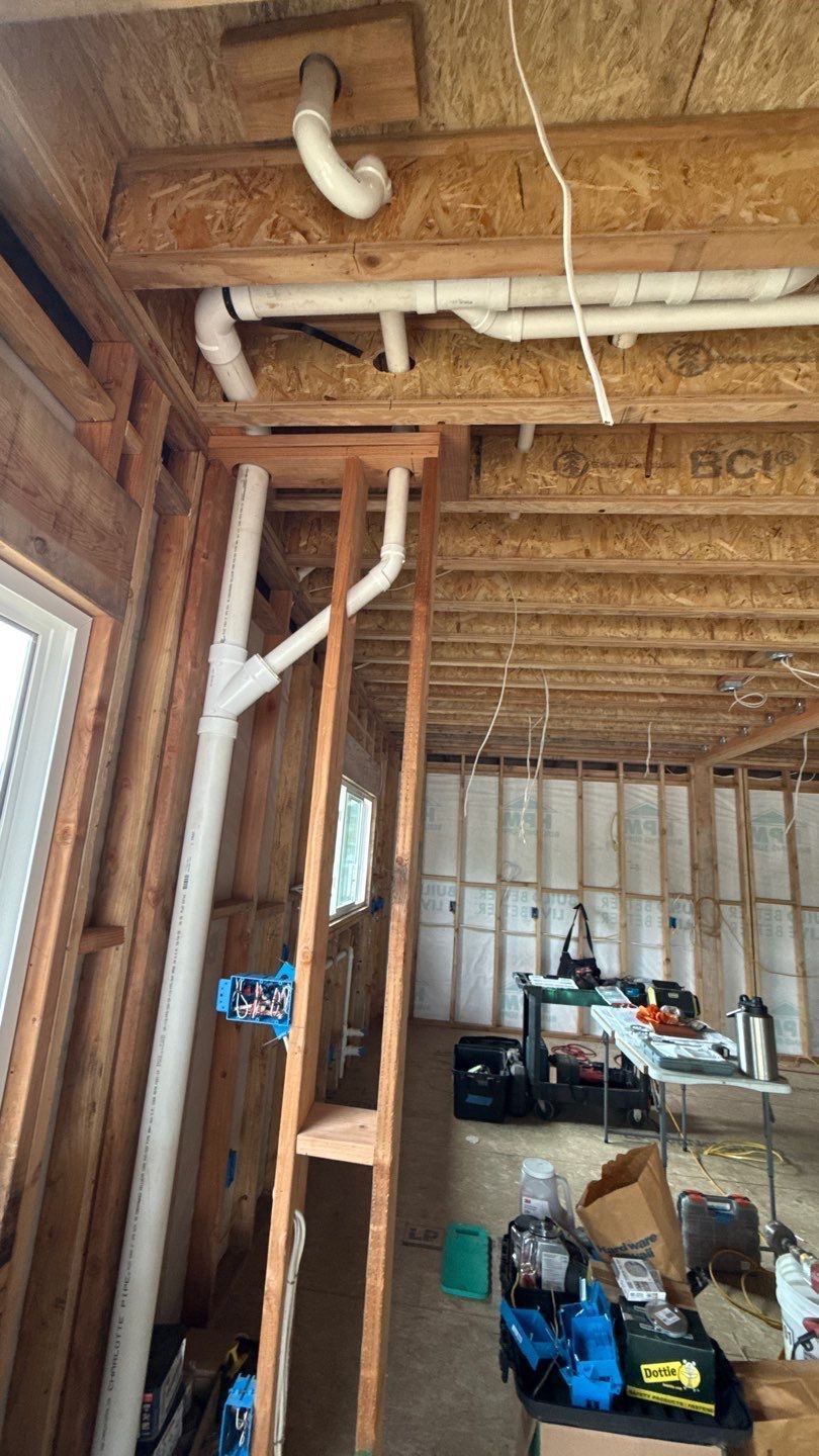 Interior of a house under construction, with exposed wooden framing, wiring, and tools on the floor.