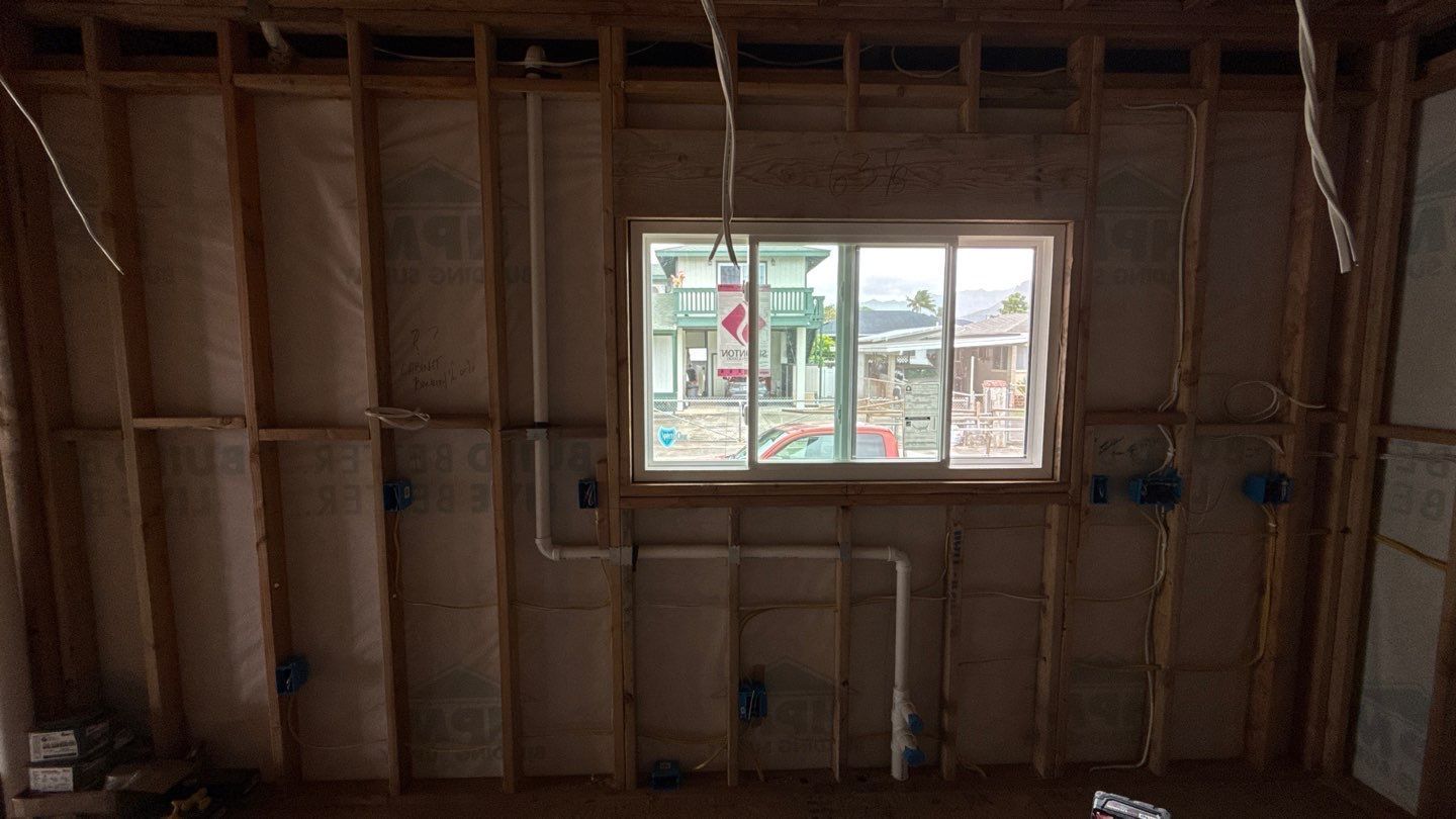 Unfinished interior wall framing with exposed studs and a window centered on the wall