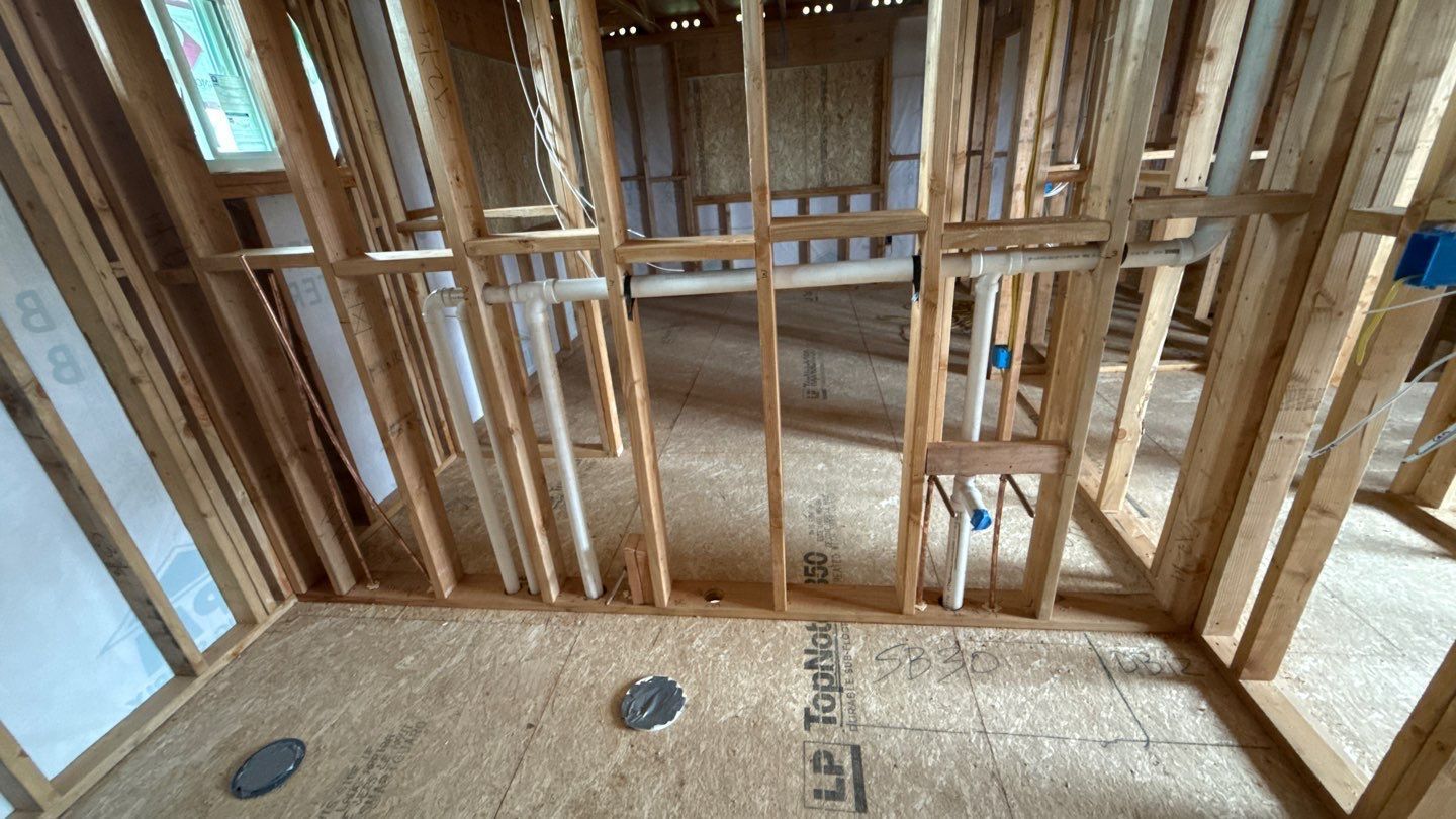 Interior wall framing under construction with exposed wood studs and plywood subfloor.