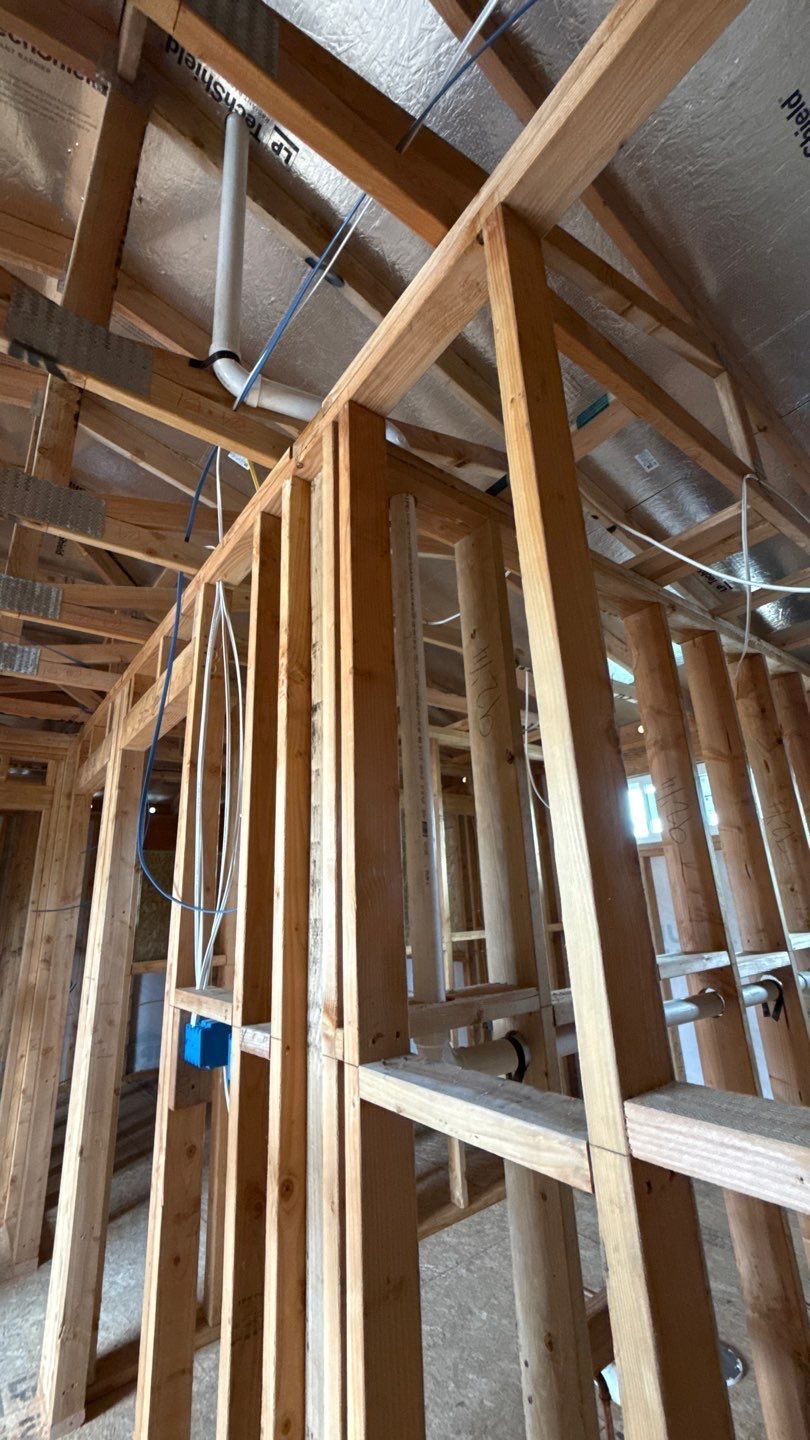 Interior of a house under construction, showing wooden framing and exposed roof trusses.
