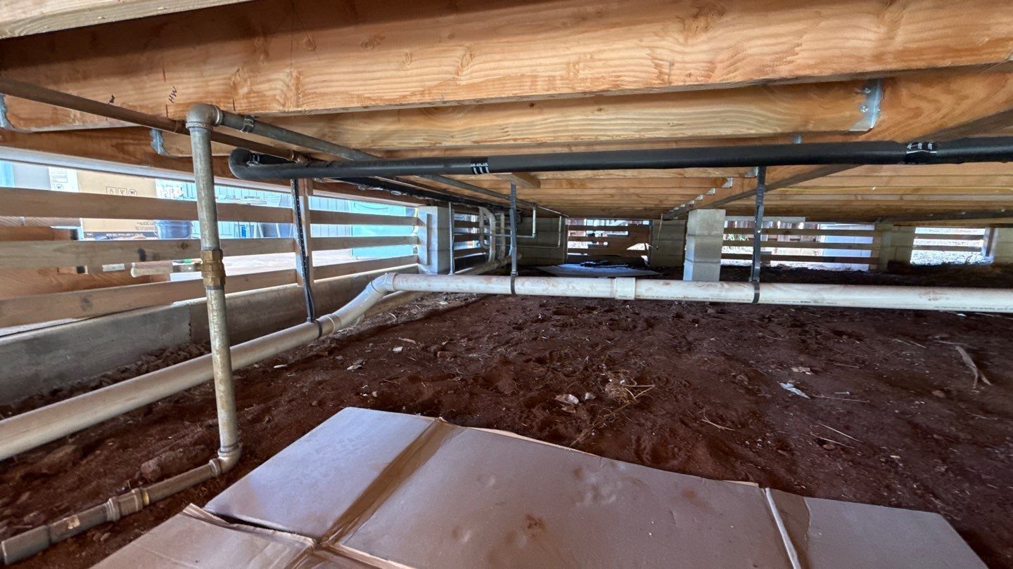 Under-bed storage space with dirt floor, low wooden beams, and corrugated metal siding