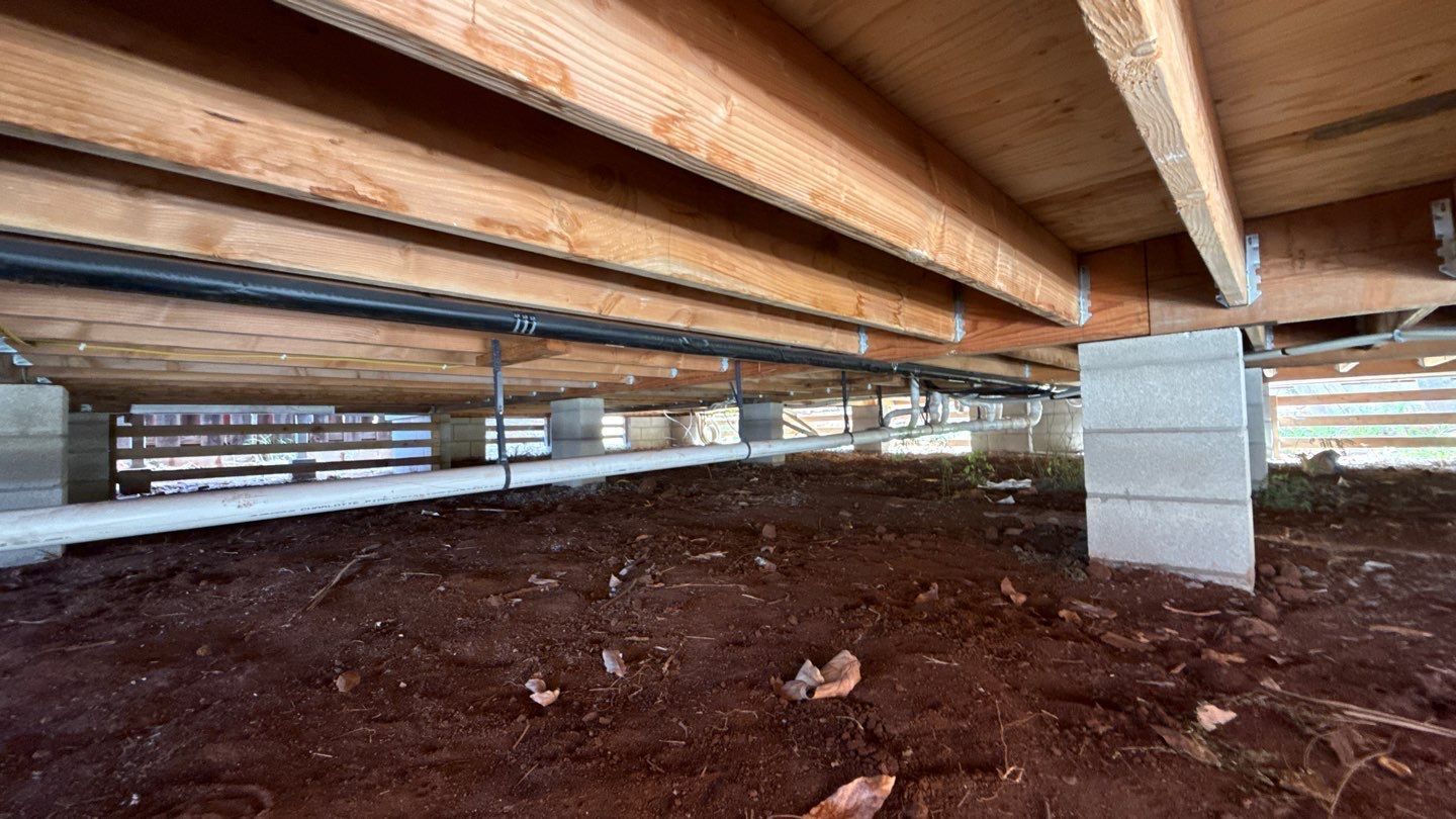 Low crawl space under a wooden building with exposed beams and a concrete support pillar.