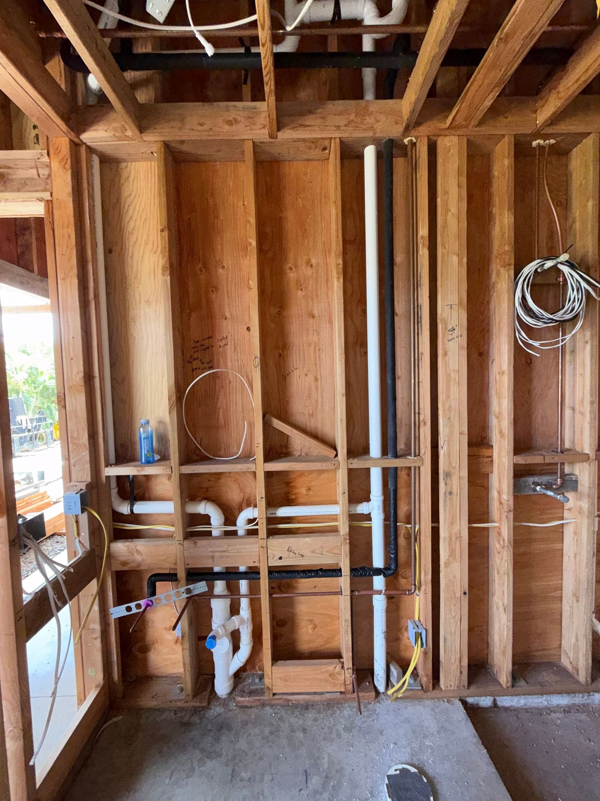 Framed house wall with exposed studs, plumbing pipes, and electrical wiring in an unfinished interior