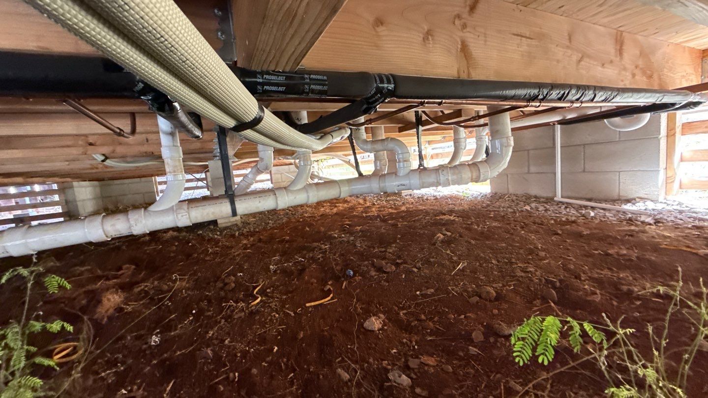 Crawlspace with exposed ducts and pipes above a dirt floor beneath wooden beams