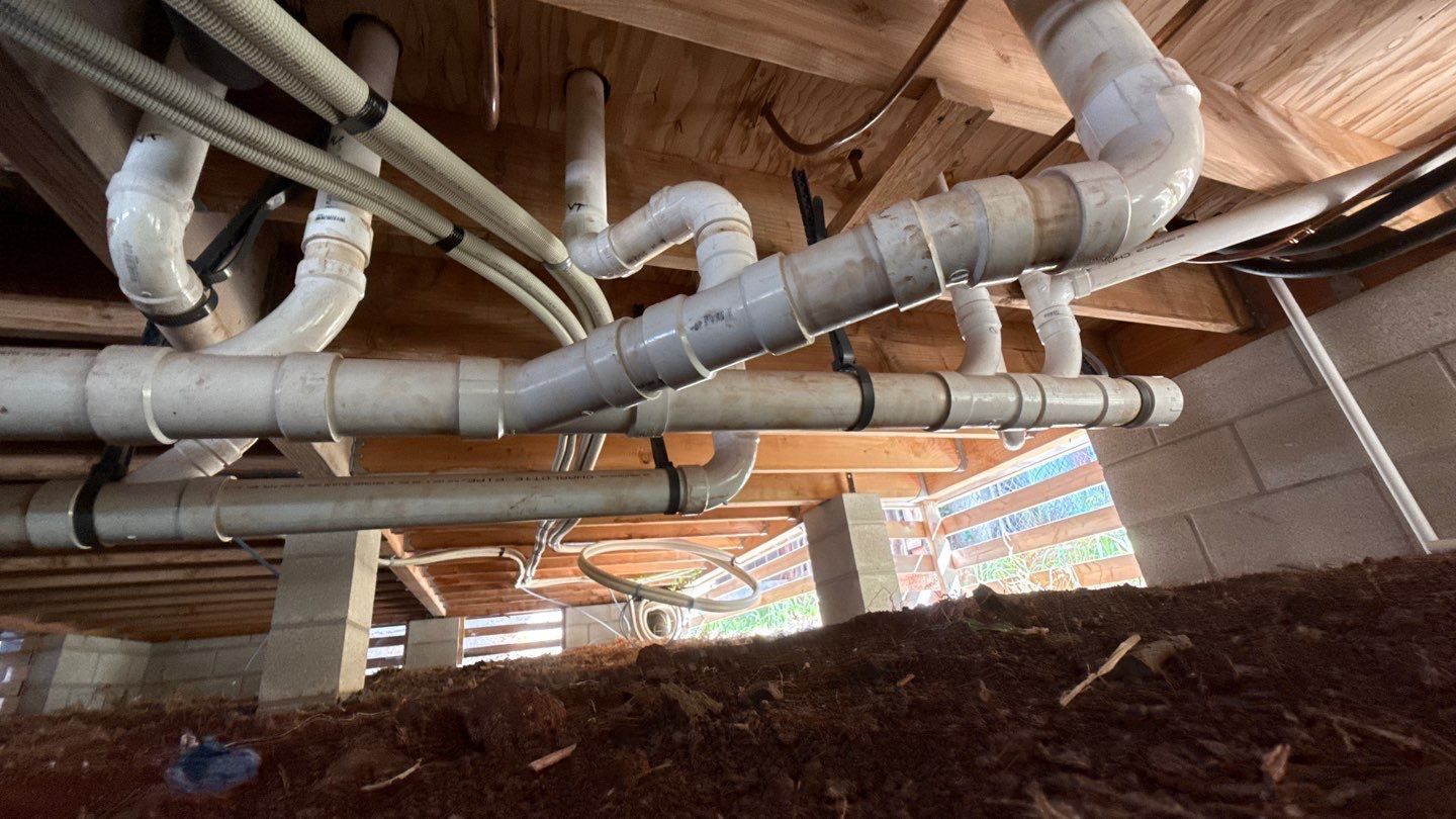 Exposed silver ventilation ducts and pipes running beneath a wooden ceiling in an attic or crawlspace