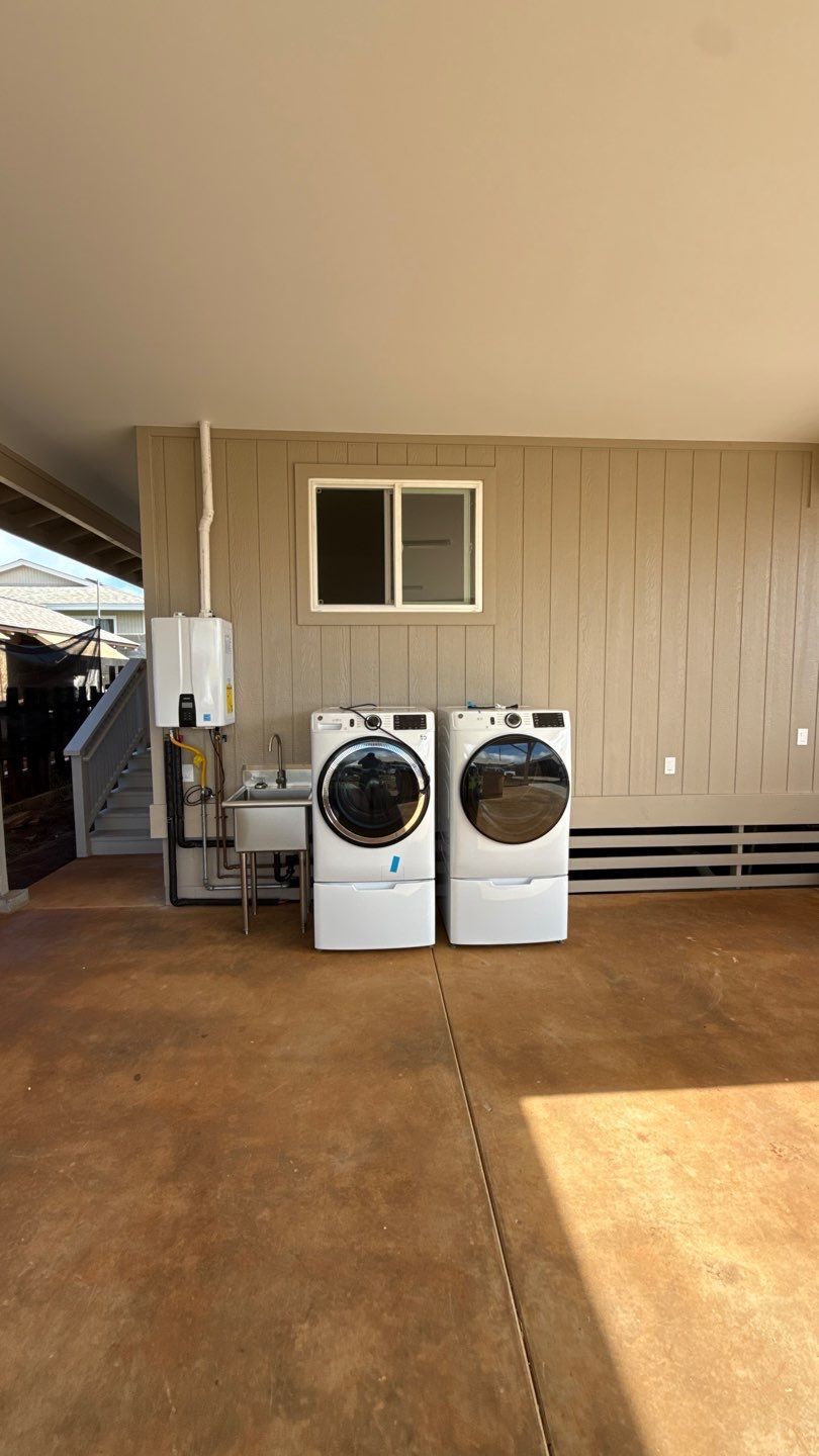 Two front-loading laundry machines on a concrete patio beside a beige house wall.