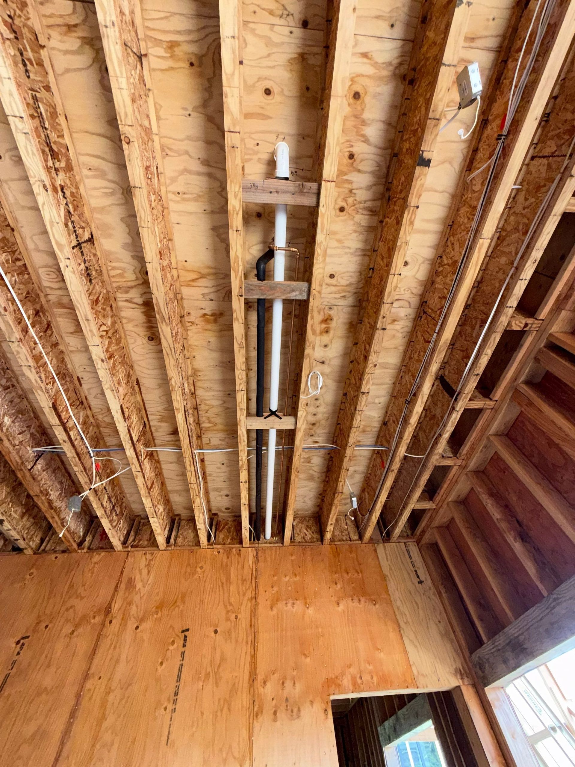 Exposed wooden ceiling joists with a central metal support, viewed from inside an unfinished room.