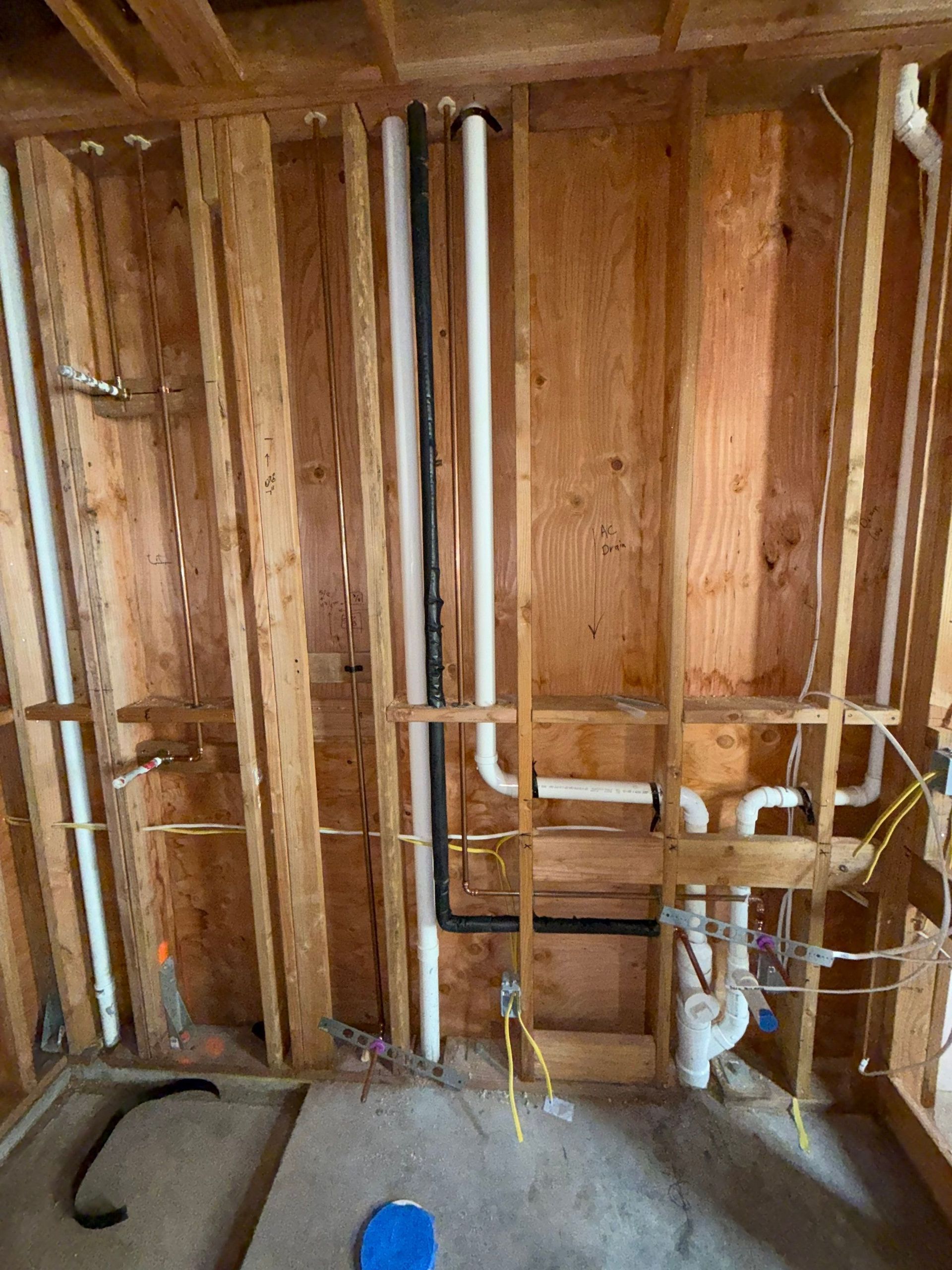 Partially framed bathroom wall with exposed plumbing pipes and studs during renovation