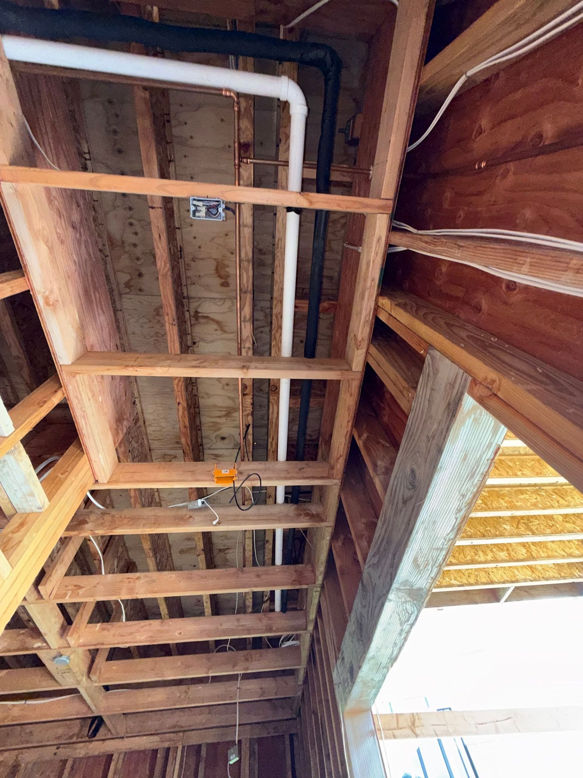 Exposed wooden ceiling joists with white pipes and a large bright skylight opening on the right.