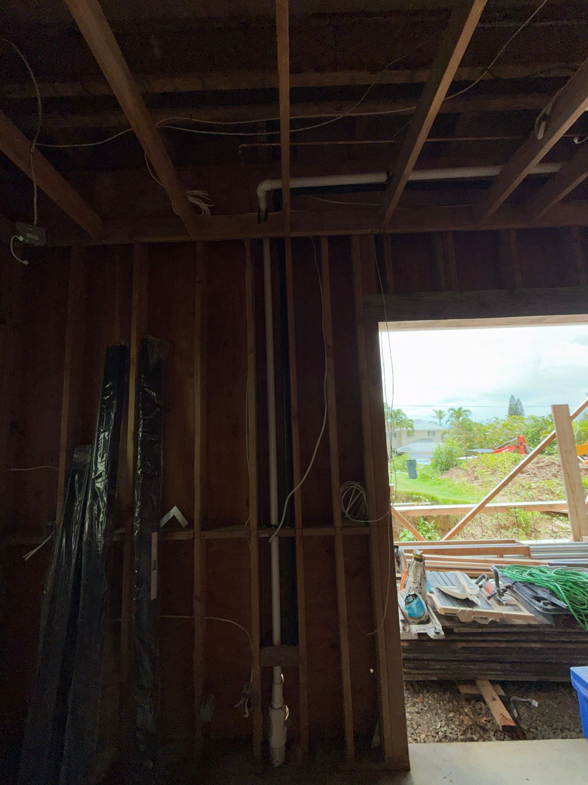 Inside a wooden-framed room under construction, looking out through an open doorway to a bright outdoor site.