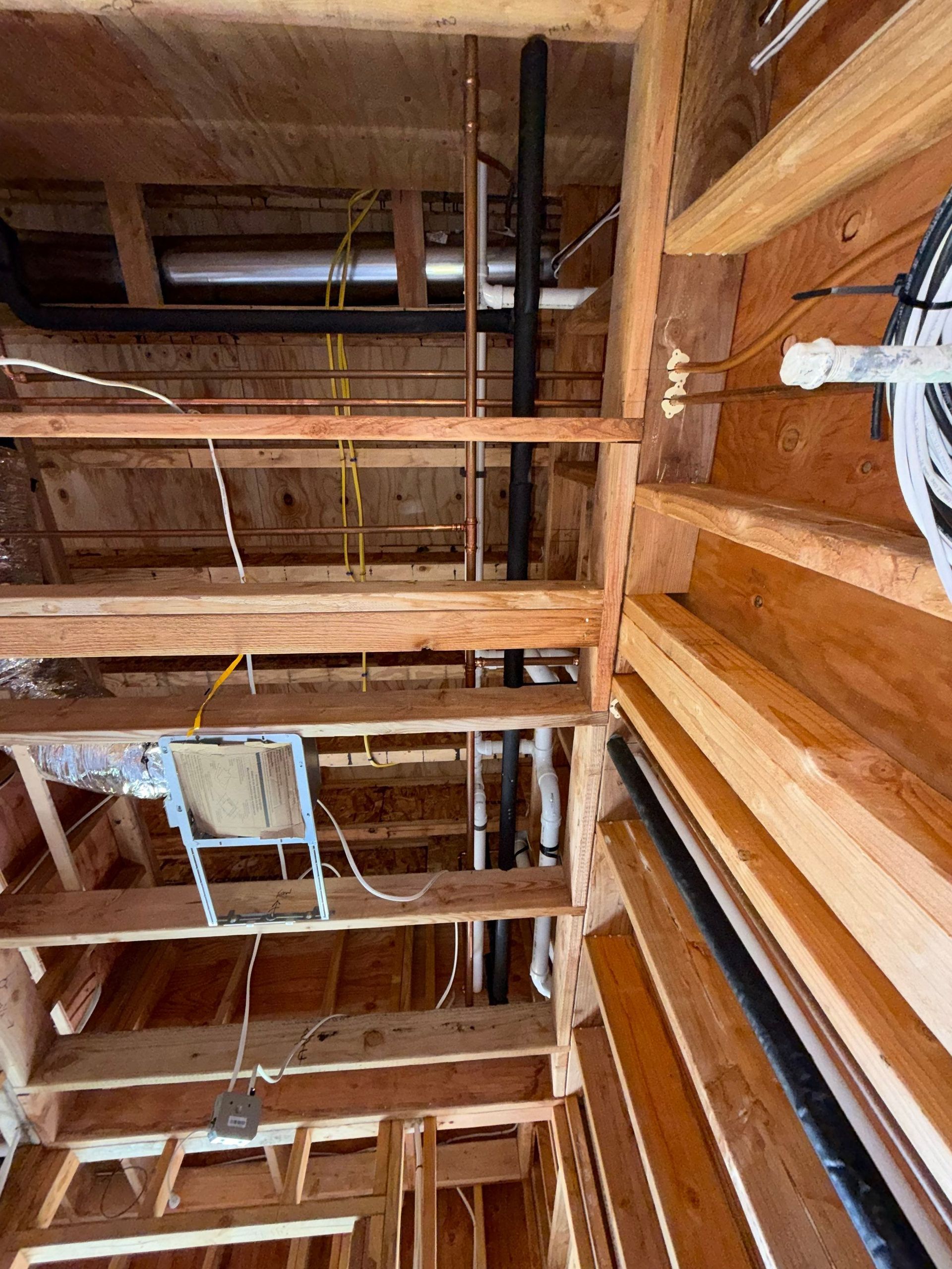 Unfinished wooden attic framing with exposed beams, pipes, and insulation under construction