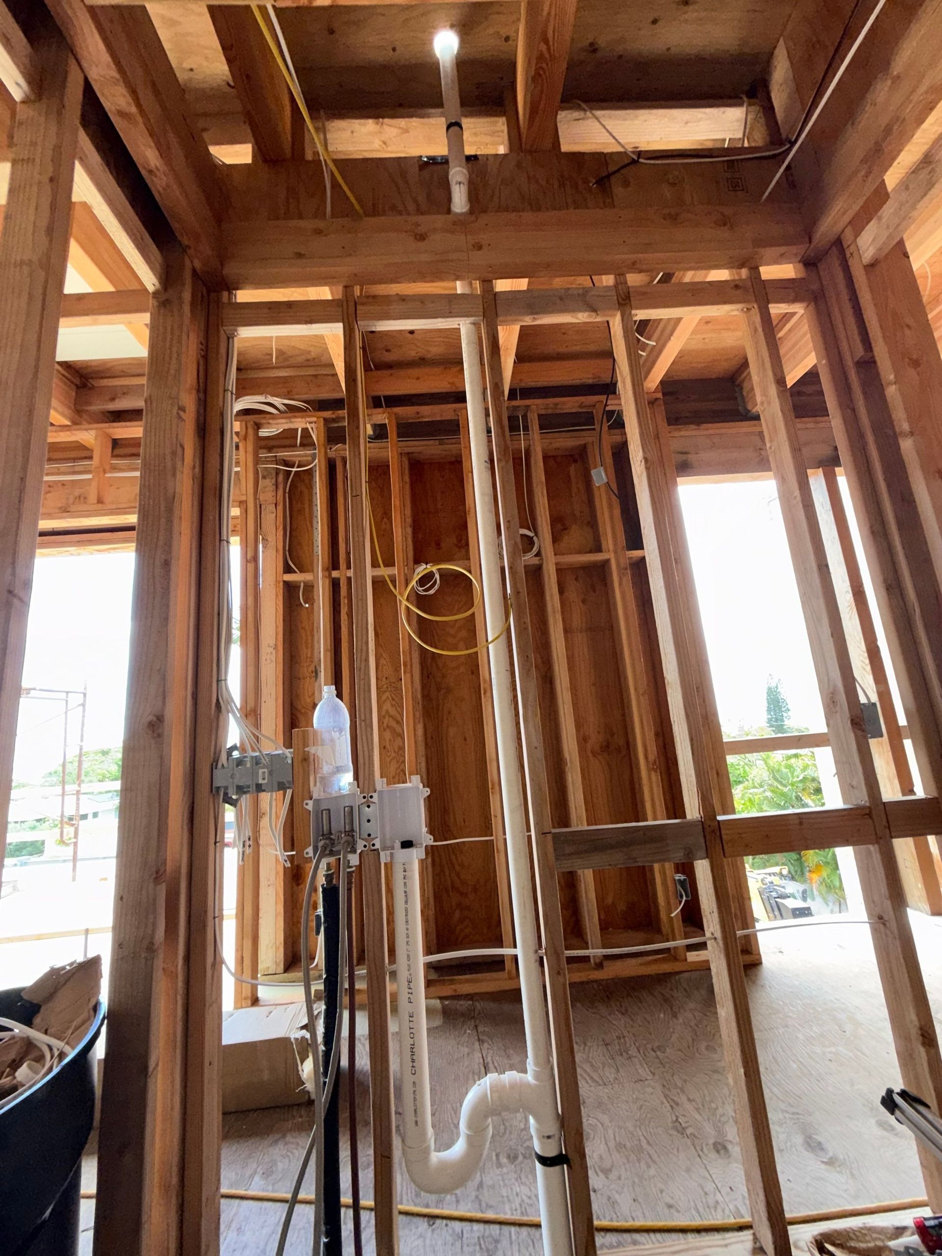 Wood-framed construction site interior with exposed studs and plumbing pipes in progress
