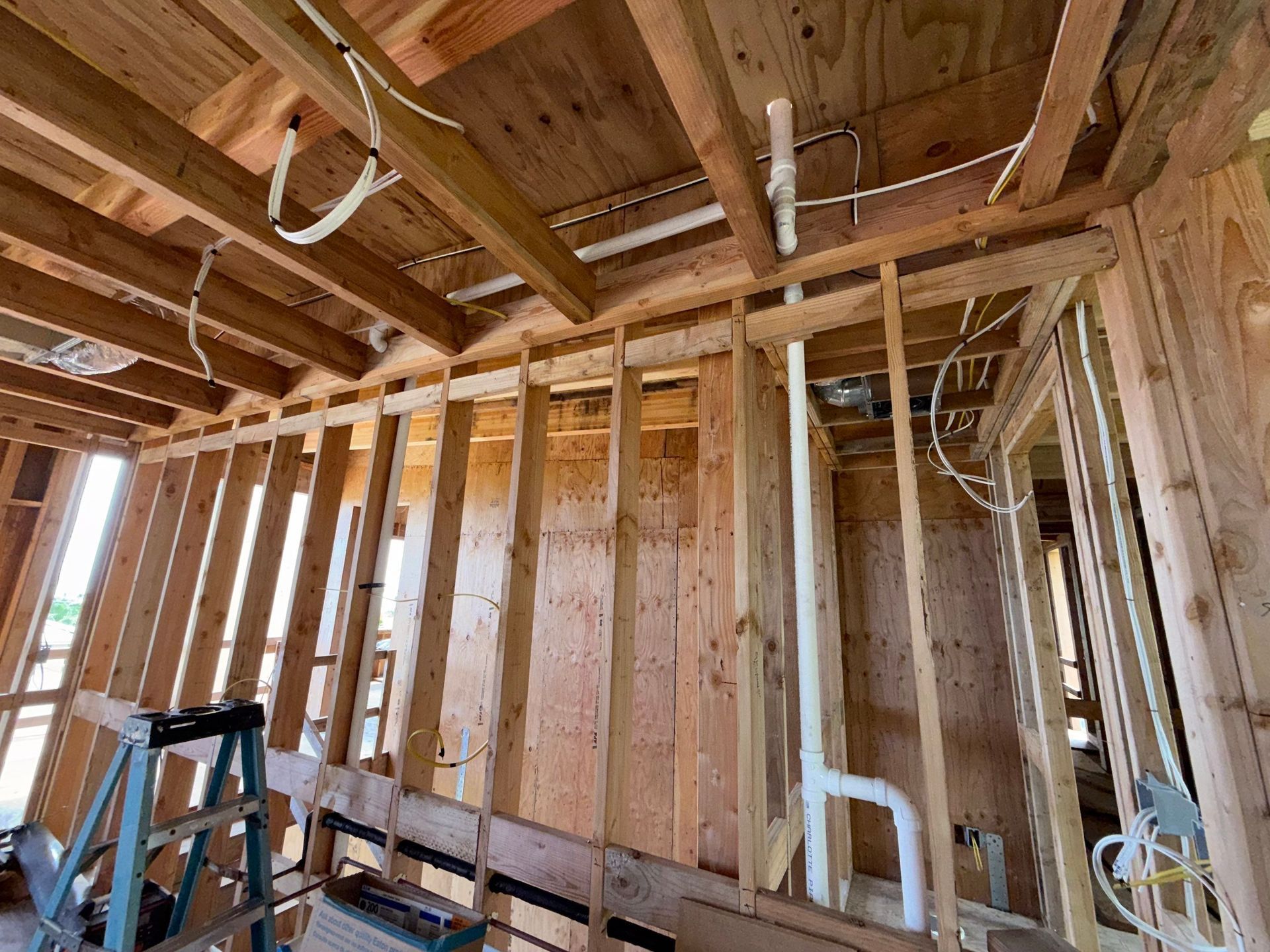 Interior of a framed house under construction, with exposed wooden studs, ceiling joists, and a ladder.