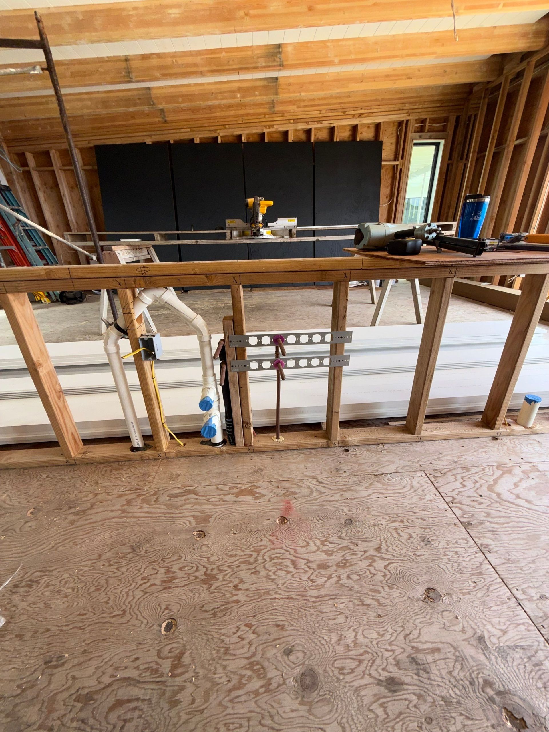 Unfinished interior with exposed wooden framing, staircase opening, and construction tools in a partially built room