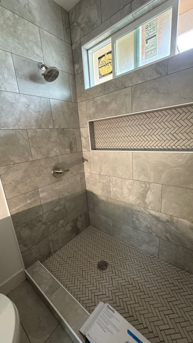 Walk-in tiled shower with two wall-mounted showerheads, window, and floor drain