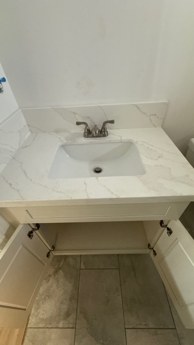 Small white bathroom sink with chrome faucet and vanity cabinet beneath, set against tiled walls and floor.