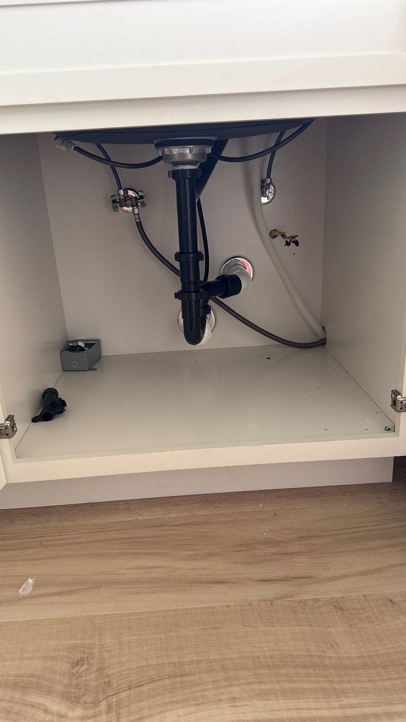 Under-sink cabinet with exposed plumbing and pipes, white interior, and wood flooring below