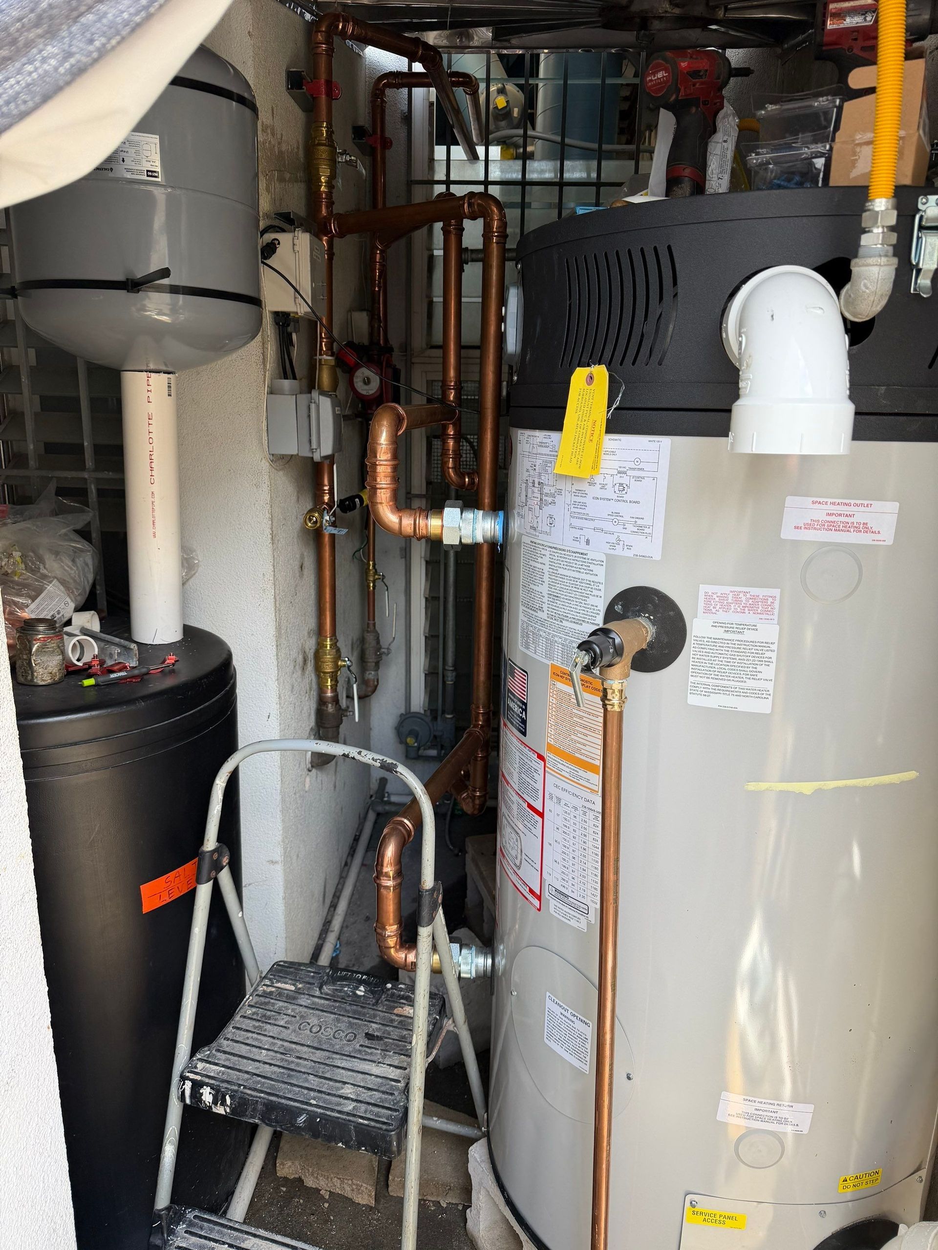 Utility room with water heater, pipes, and a furnace beside metal stairs