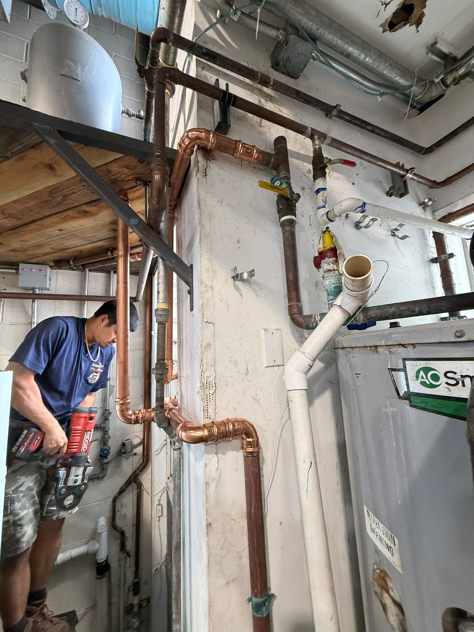 Worker fixing copper pipes in a utility room with exposed ceiling and plumbing fixtures