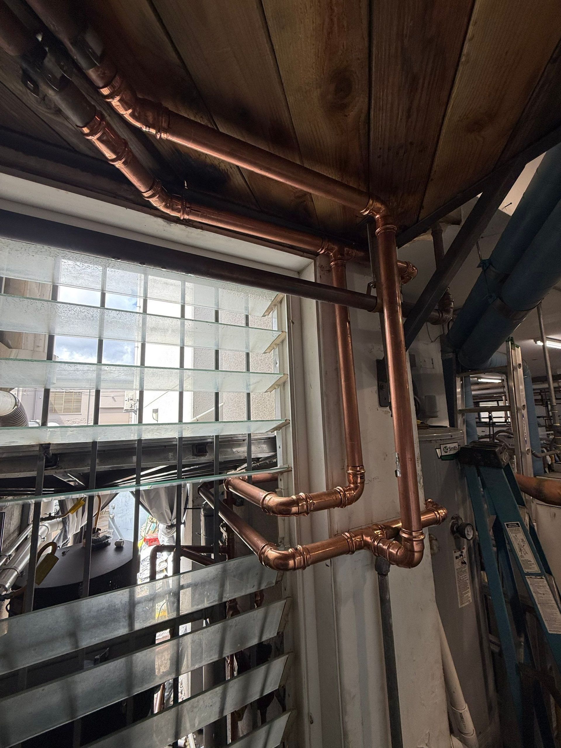 Copper pipes and metal beams under a roof, viewed inside an industrial structure.