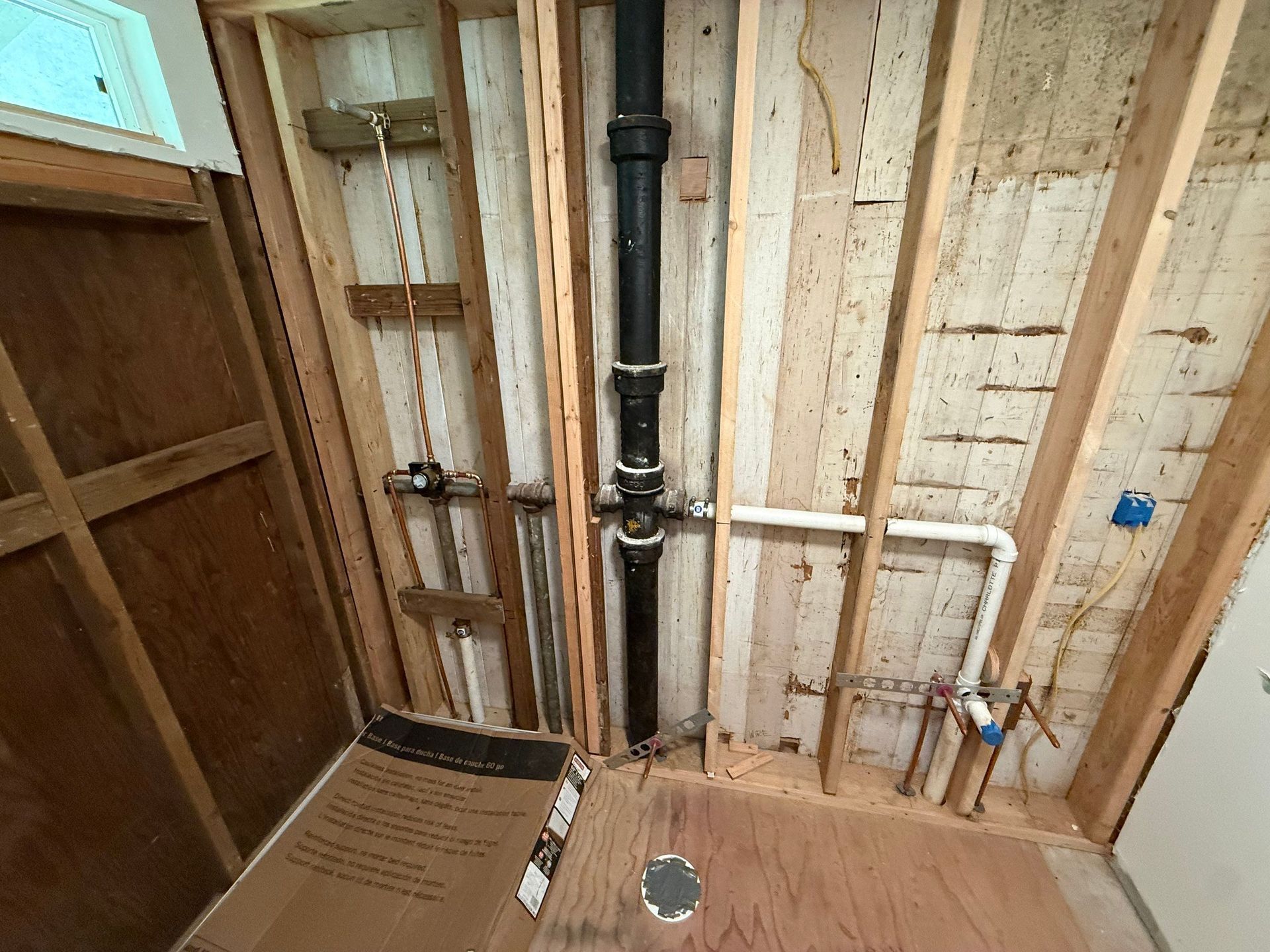 Unfinished bathroom wall with exposed plumbing, a black vent pipe, and cardboard on the floor.