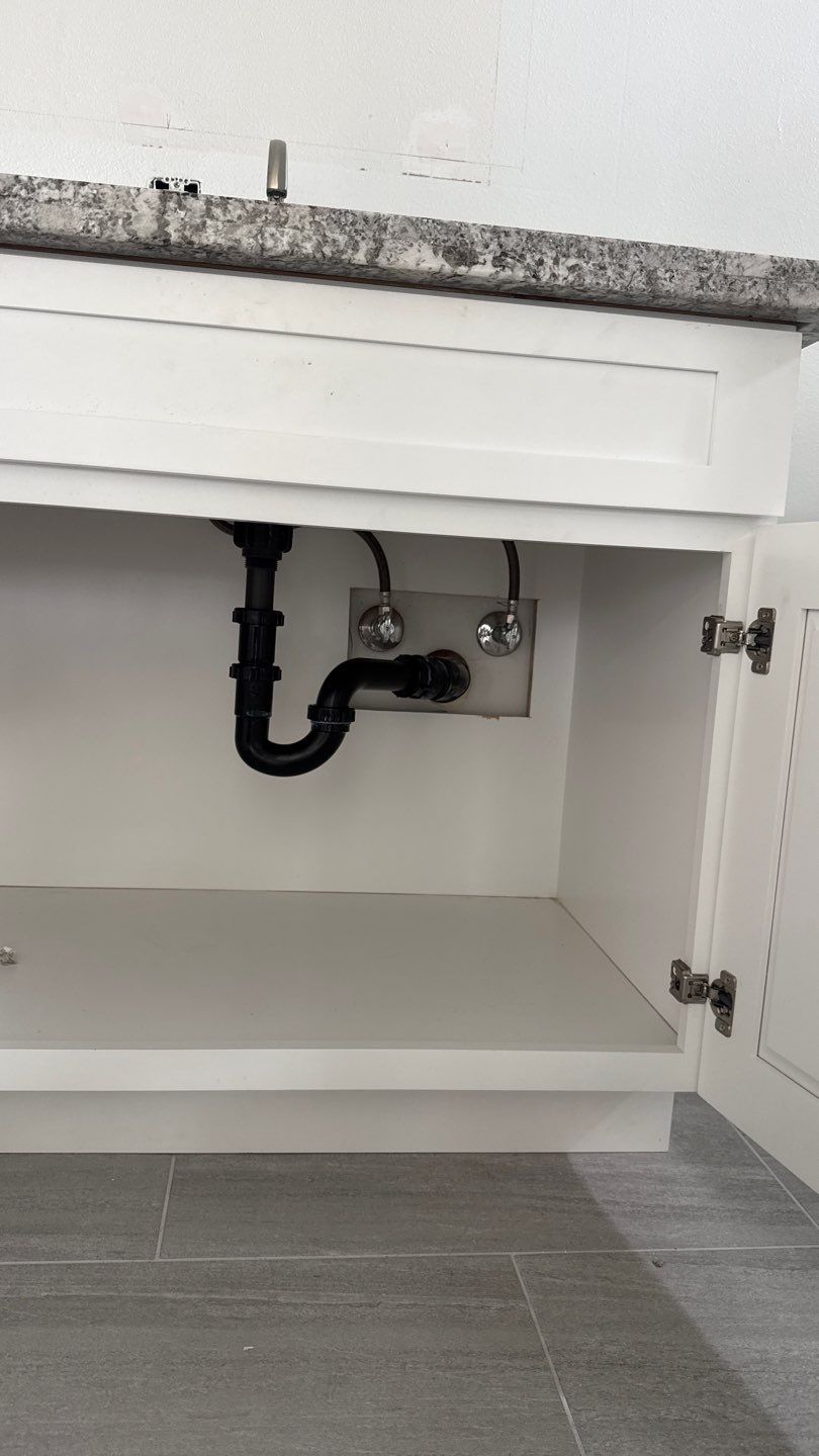 Open cabinet under sink showing black plumbing pipes and white interior shelves