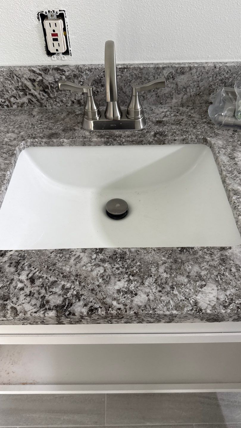 White bathroom sink with chrome faucet set in gray speckled granite countertop.