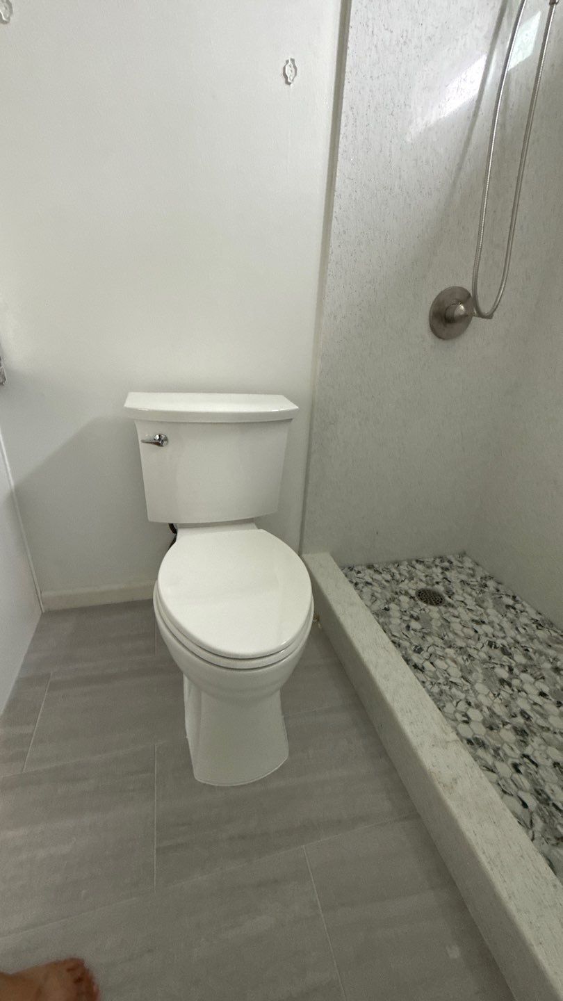 Small bathroom with a toilet beside a pebble-lined shower area and glass partition.