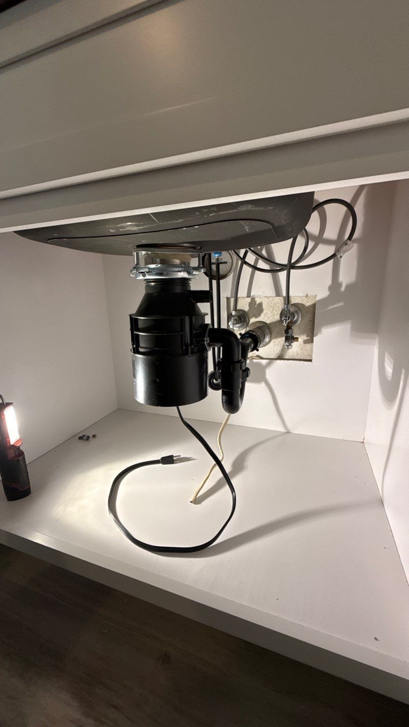 Under-sink plumbing and a garbage disposal with visible pipes and cables.