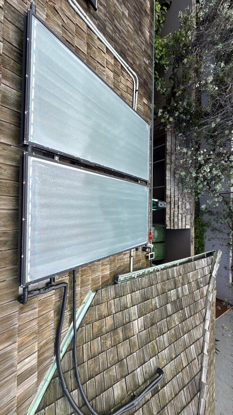 Two large silver metal panels leaning against a brick wall outdoors near a tree and coiled hose