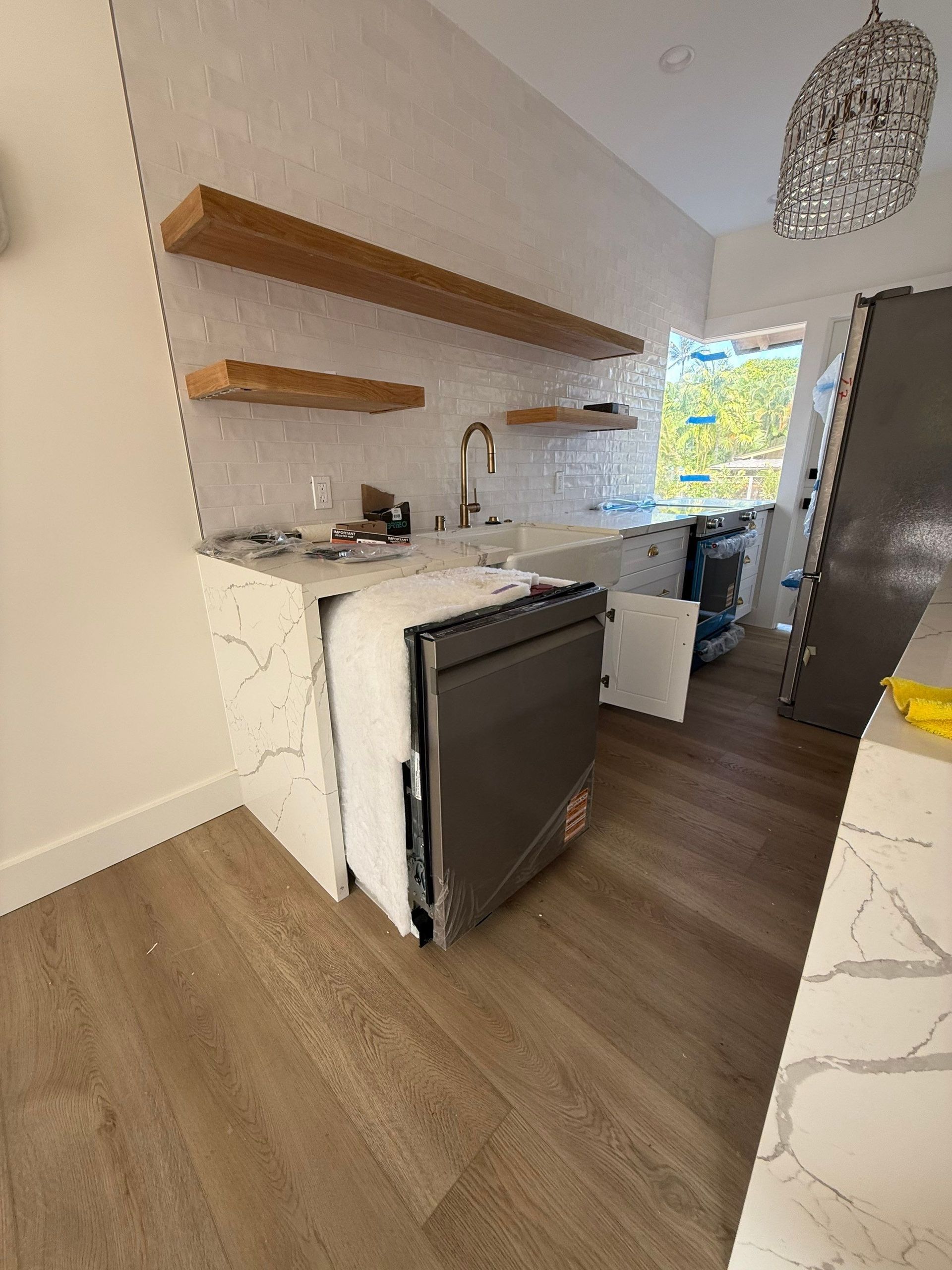 Modern kitchen with wood shelves, black dishwasher, white cabinets, and large window.