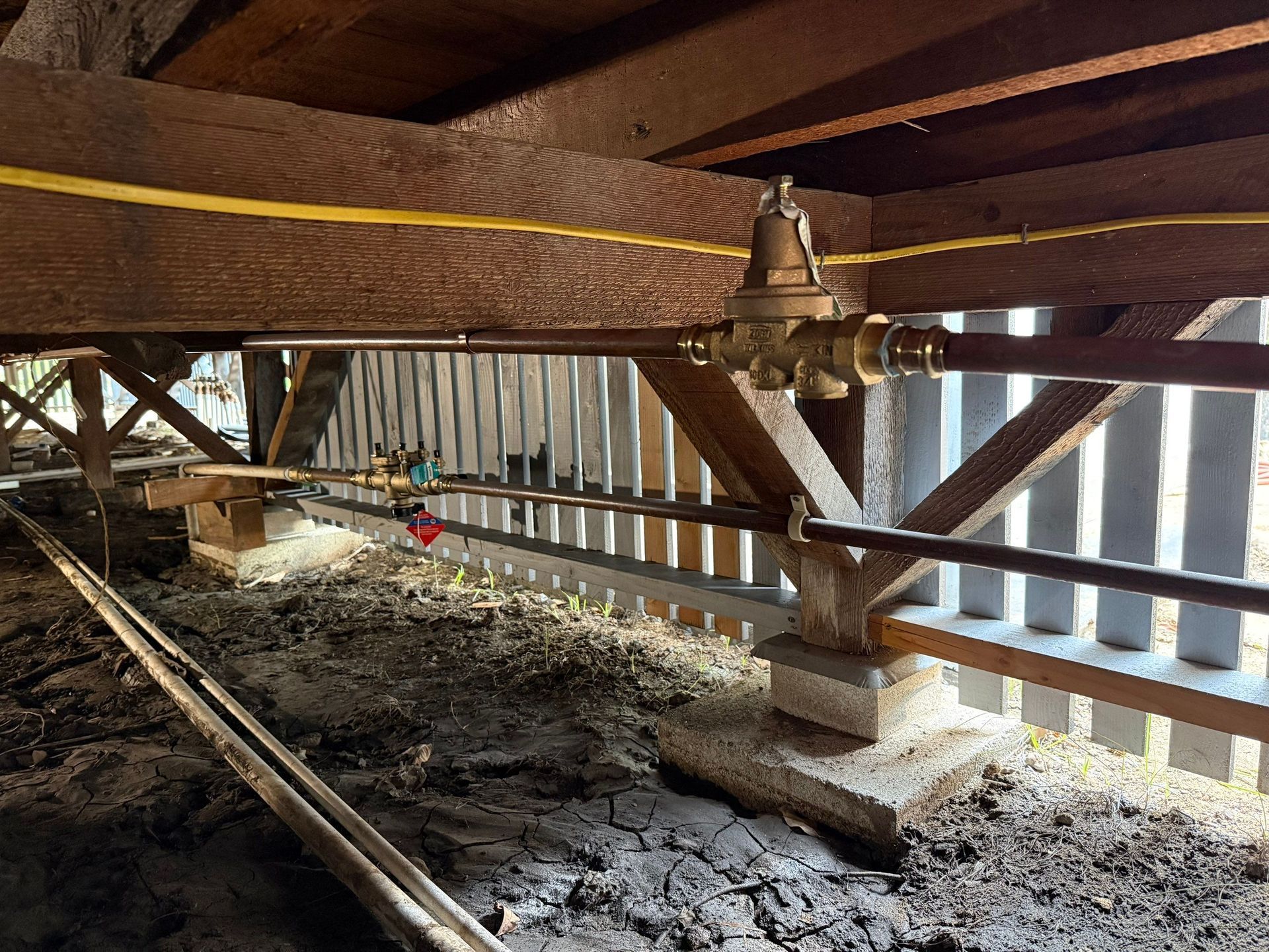 Under a wooden structure, a yellow measuring tape stretches across beams above muddy ground.