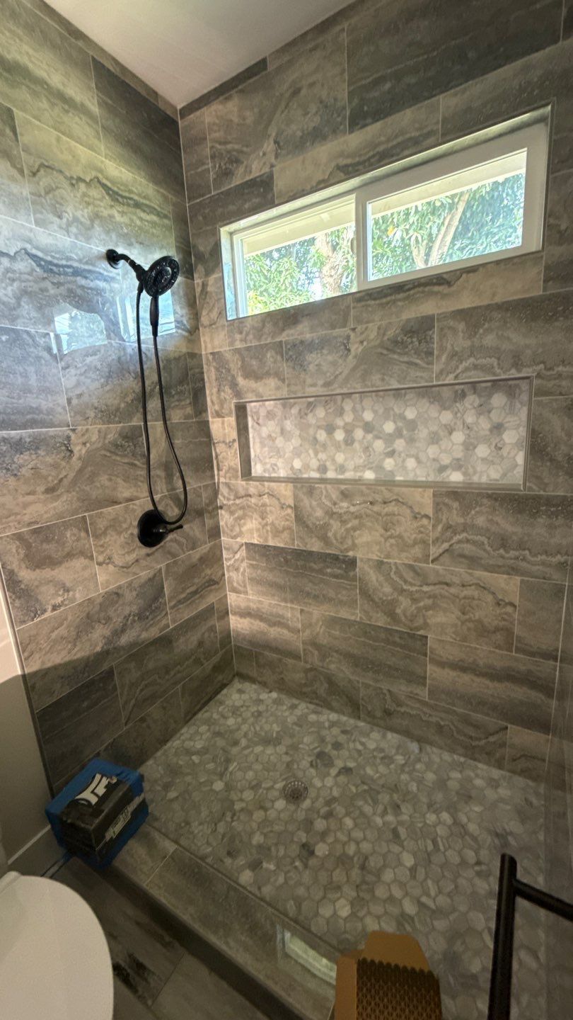 Small tiled shower with bench, black showerhead, and frosted window above.