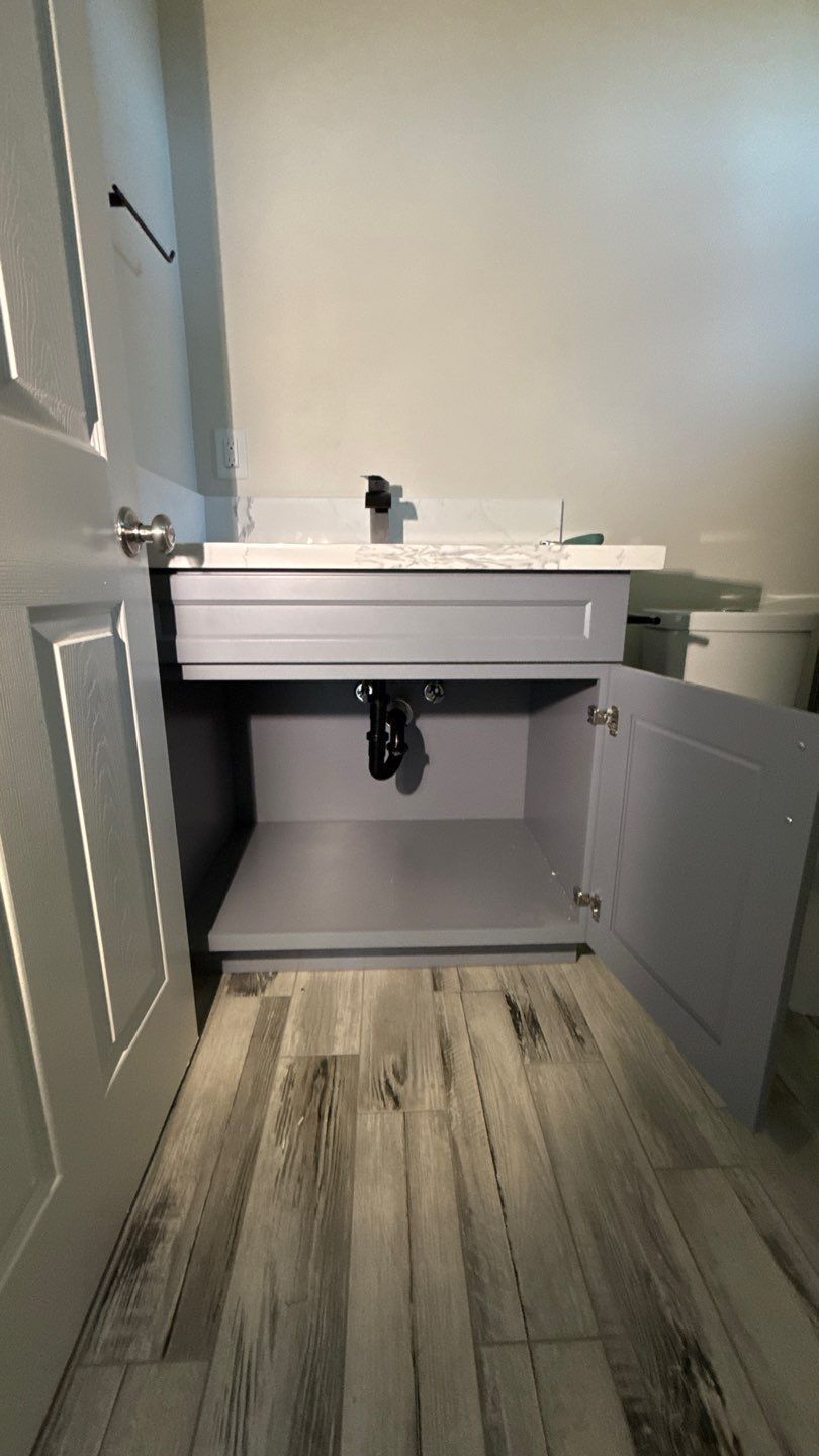 Bathroom vanity with sink and open cabinet doors over wood-look tile floor