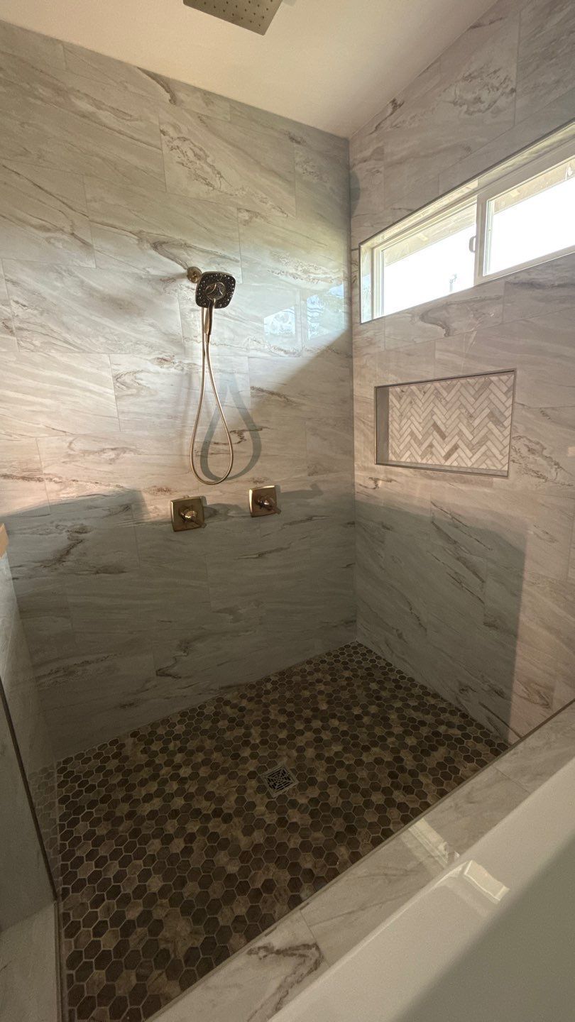 Small tiled shower with a wall-mounted showerhead, mosaic floor, and high windows.