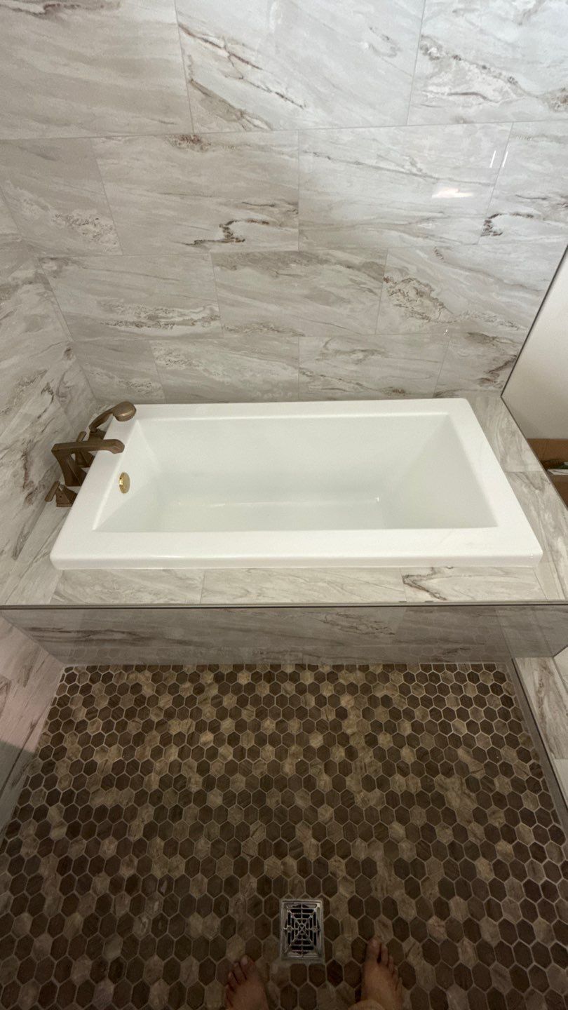 White rectangular bathtub set into a tiled alcove above a patterned mosaic floor.