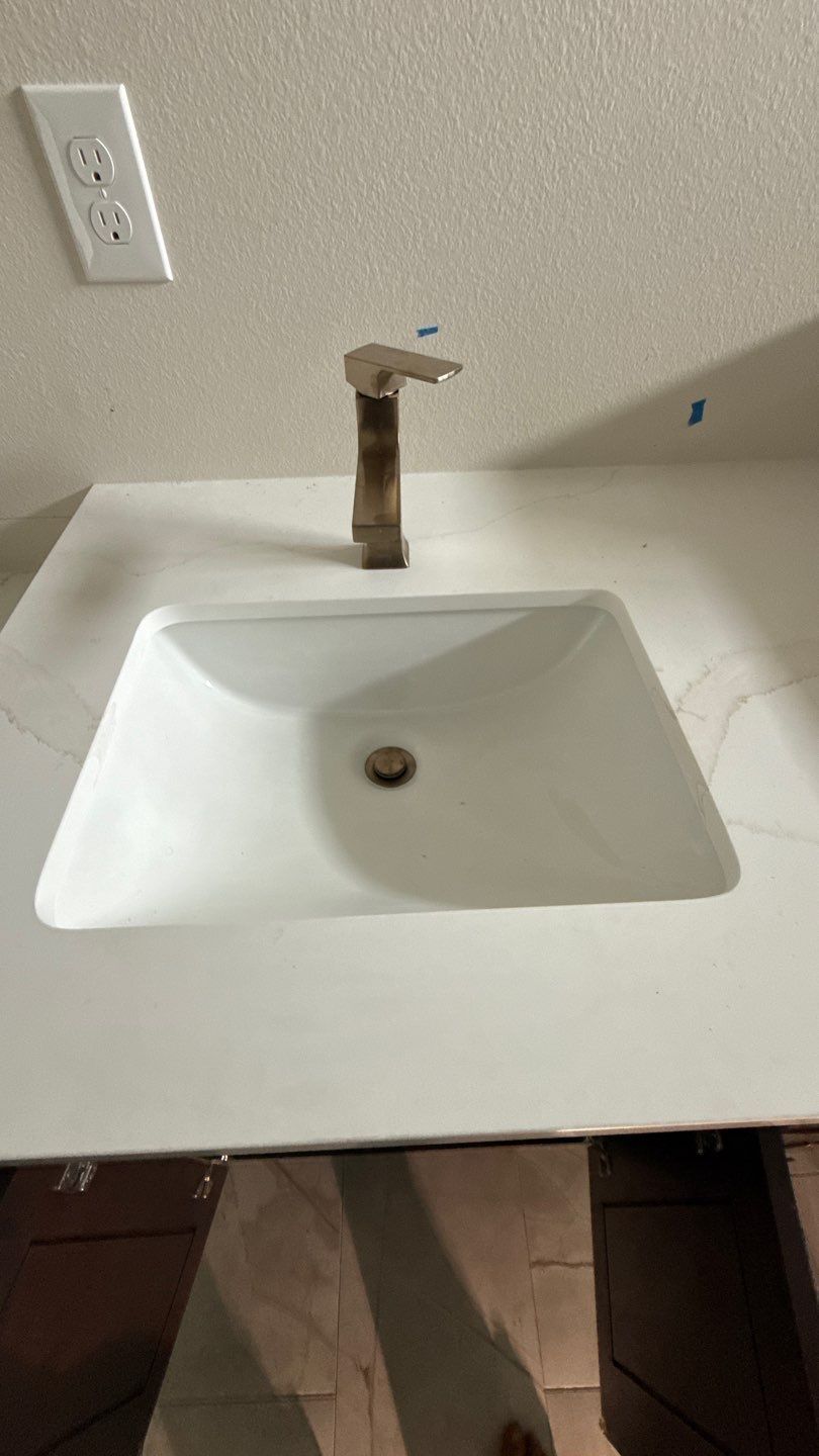 White bathroom sink with bronze faucet and countertop against a beige wall.