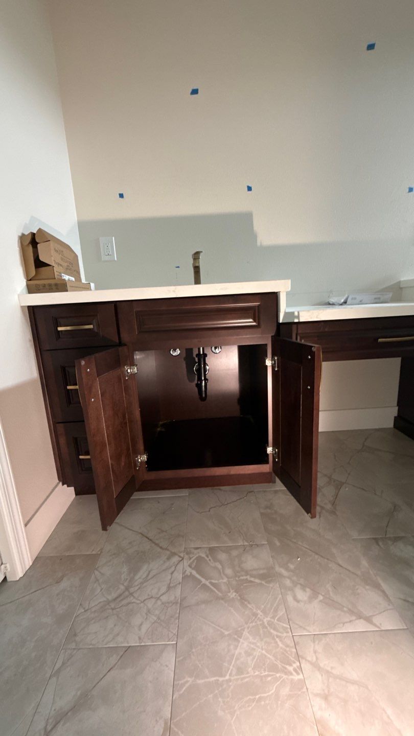 Kitchen sink cabinet with both brown doors open in a partially renovated room.