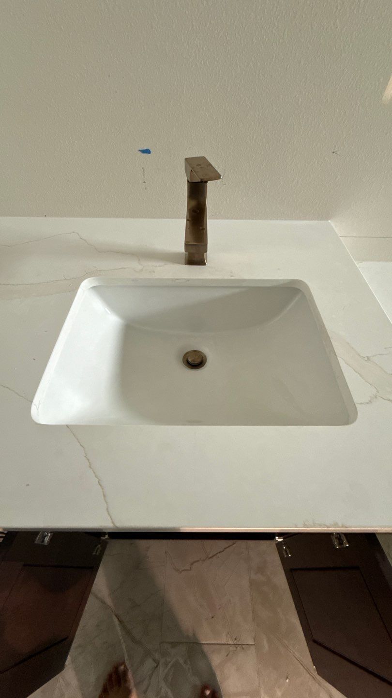 Modern white bathroom sink with brass faucet and a central drain, seen from above