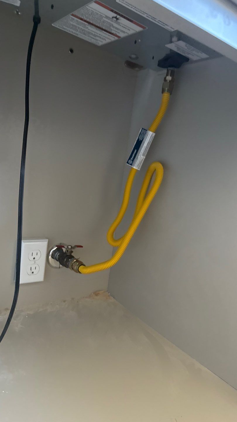Yellow gas line under a desk in a cabinet, with a wall outlet on the left.