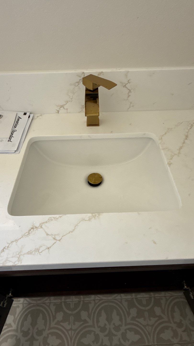 Gold faucet over white rectangular sink with gold drain and marble countertop.