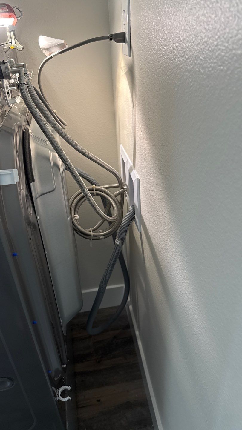 Narrow utility hallway with exposed pipes, hoses, and a white textured wall beside dark flooring.