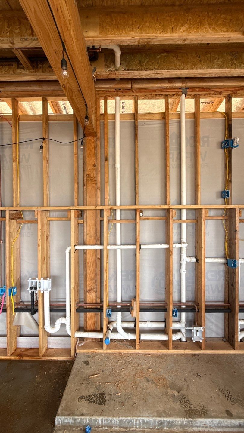 Exposed wall framing with wooden studs, insulation, and plumbing pipes in an unfinished room.