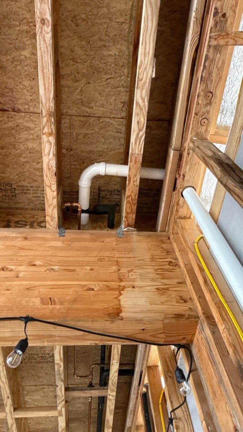 Exposed attic framing with ductwork and plumbing pipes above a wood beam and hanging light fixture