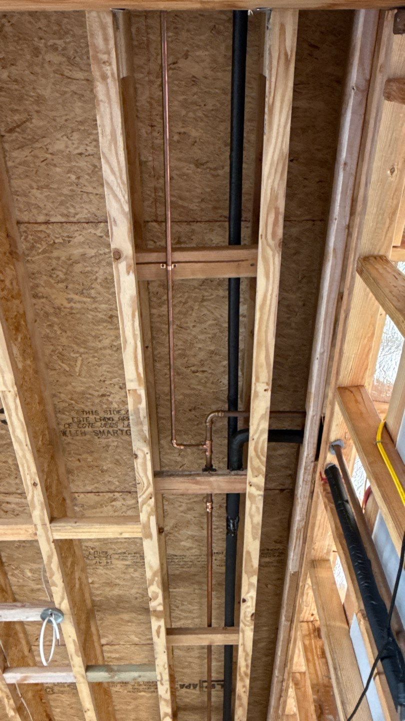 Exposed wooden ceiling framing with beams, insulation, and a black pipe running down the center.