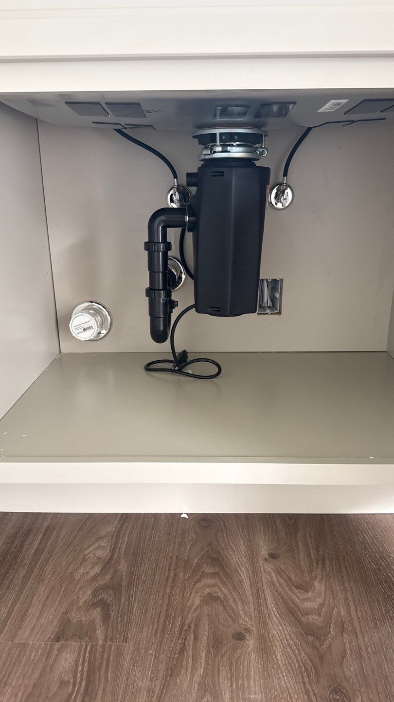 Under-sink cabinet with a black garbage disposal and plumbing pipes above a wood floor.