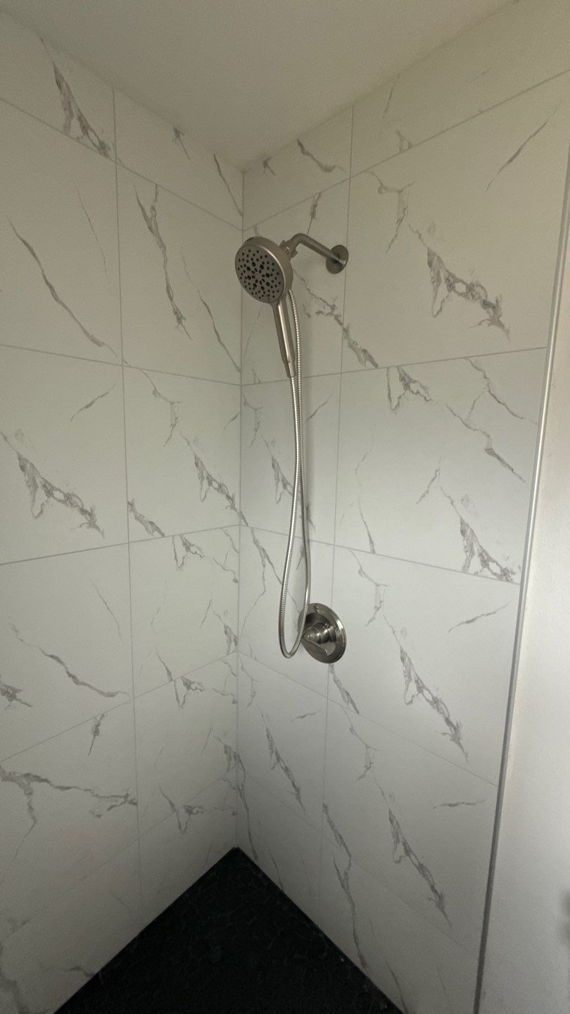 Chrome shower fixture on white marble-look tiled bathroom wall with black corner shelf